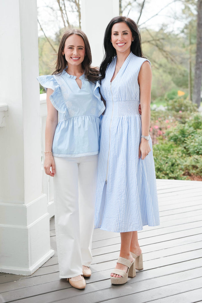 Two women in light blue tops standing on a wooden deck with a garden background