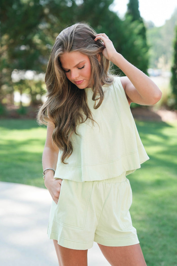 Woman in light green outfit standing outdoors with trees in the background