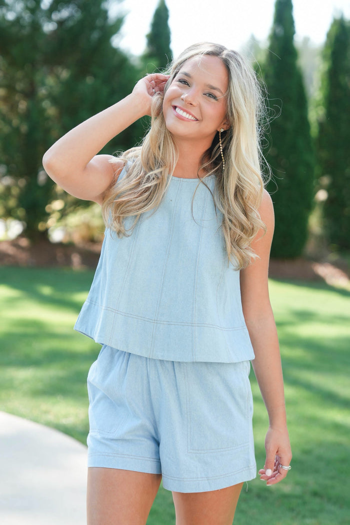 Woman wearing a light blue outfit standing outdoors with greenery in the background
