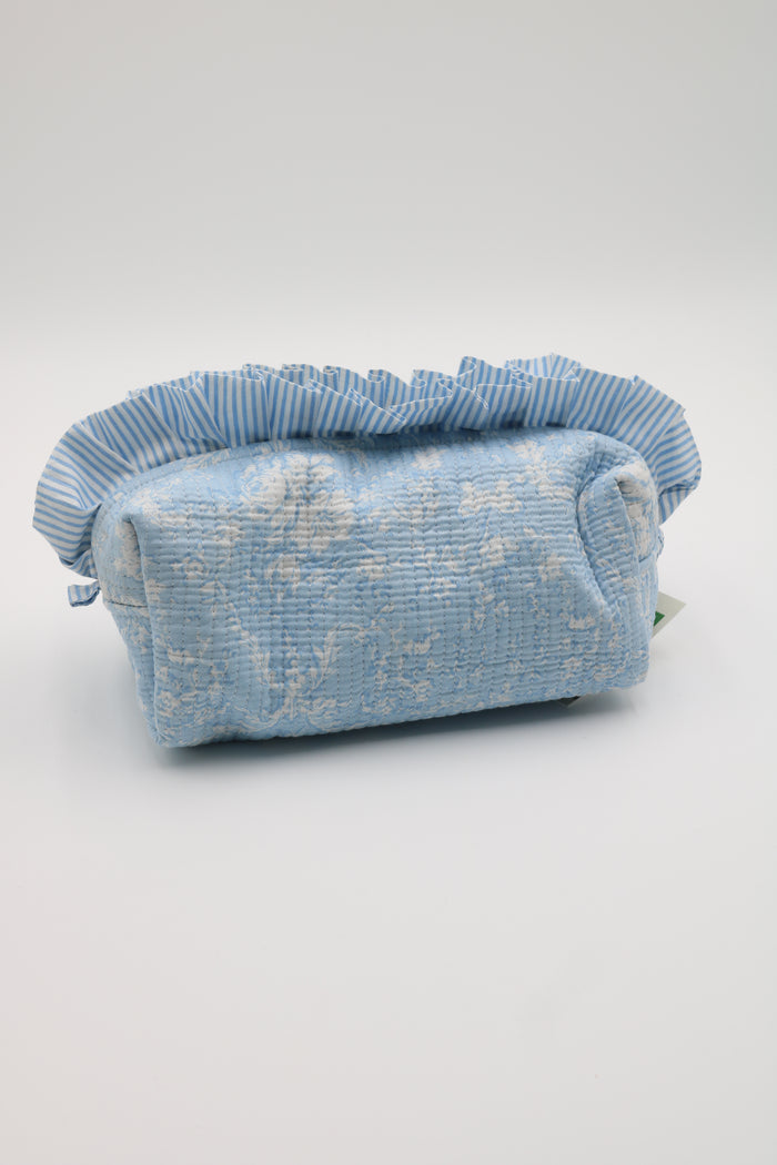 A light blue textured fabric pouch with a ruffled top trim, featuring a subtle white floral pattern, photographed on a neutral light gray background.