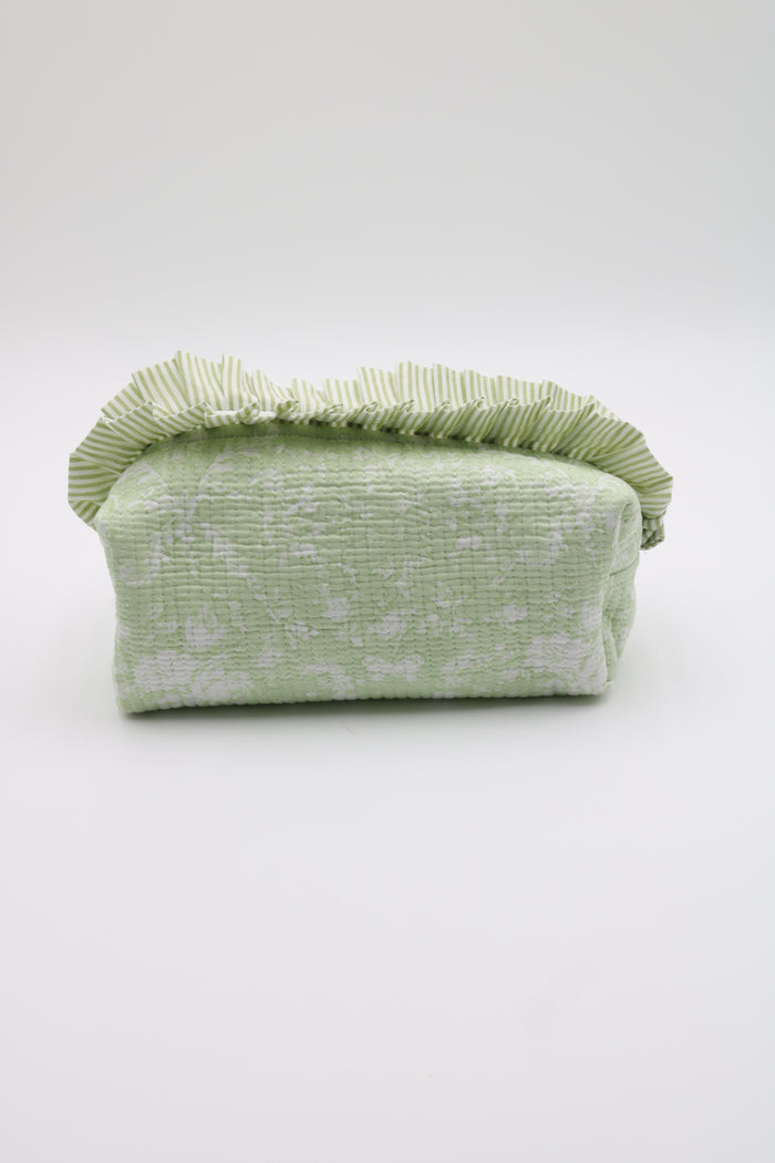 A light green textured fabric pouch with a ruffled top edge, photographed against a plain light gray studio background.