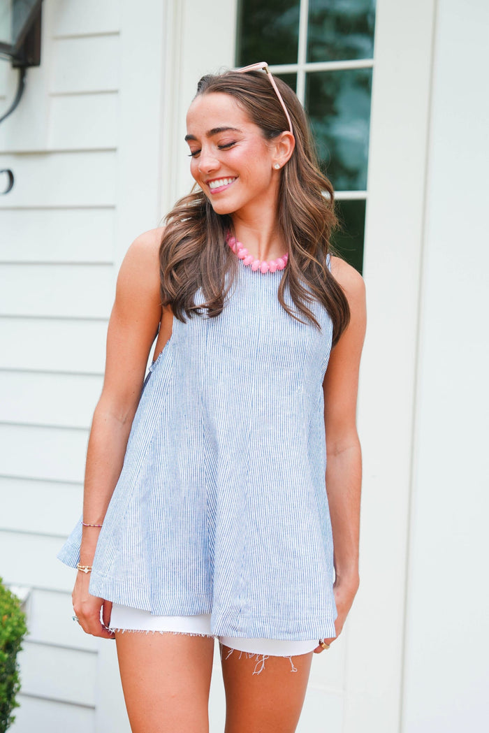Woman wearing a light blue sleeveless dress with white shorts, standing outdoors.