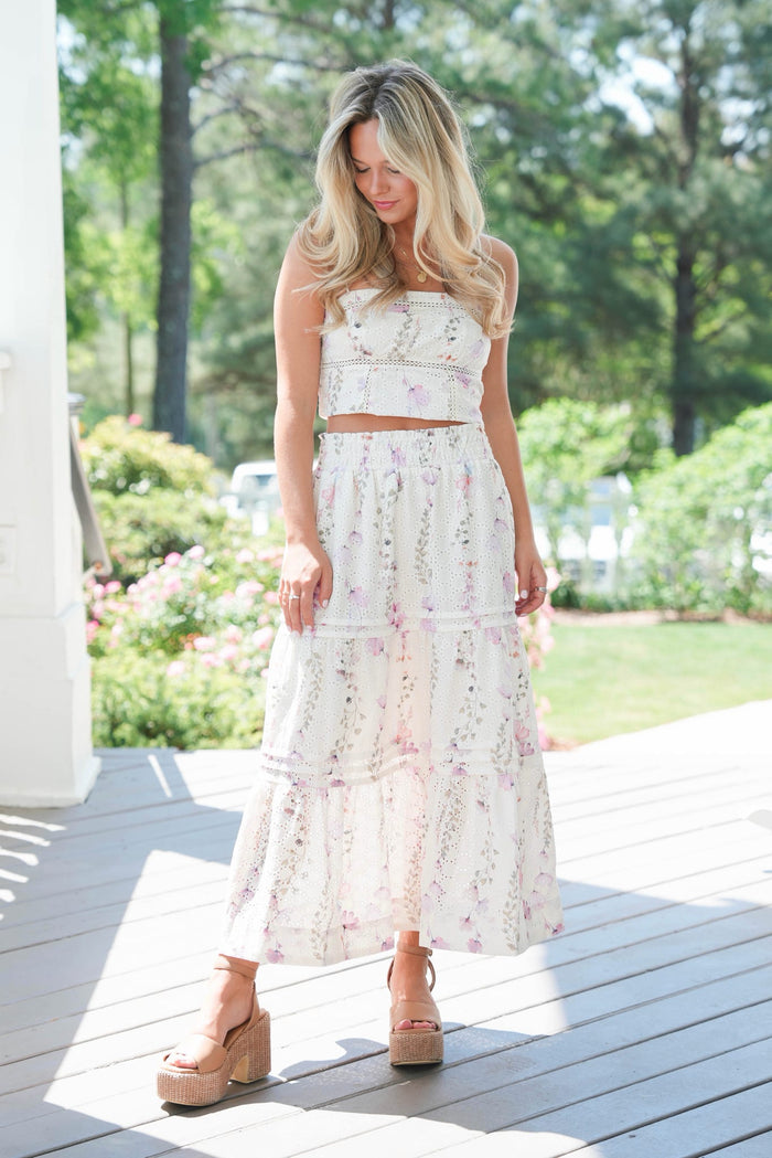 Woman in a floral dress standing on a wooden deck with greenery in the background
