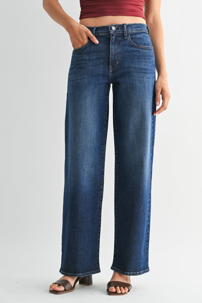 A person wearing high-waisted, wide-leg blue denim jeans with a faded wash, paired with brown slide sandals and a dark red cropped top, shown against a light gray studio background.