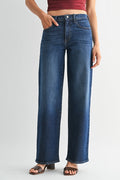 A person wearing high-waisted, wide-leg blue denim jeans with a faded wash, paired with brown slide sandals and a dark red cropped top, shown against a light gray studio background.