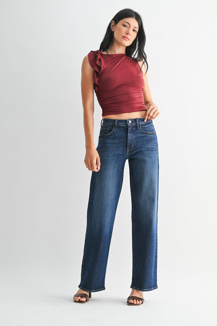 A woman modeling a sleeveless maroon crop top and dark blue wide-leg jeans against a light gray studio background.