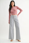 Woman wearing a pink cropped sweater and light blue jeans on a white background