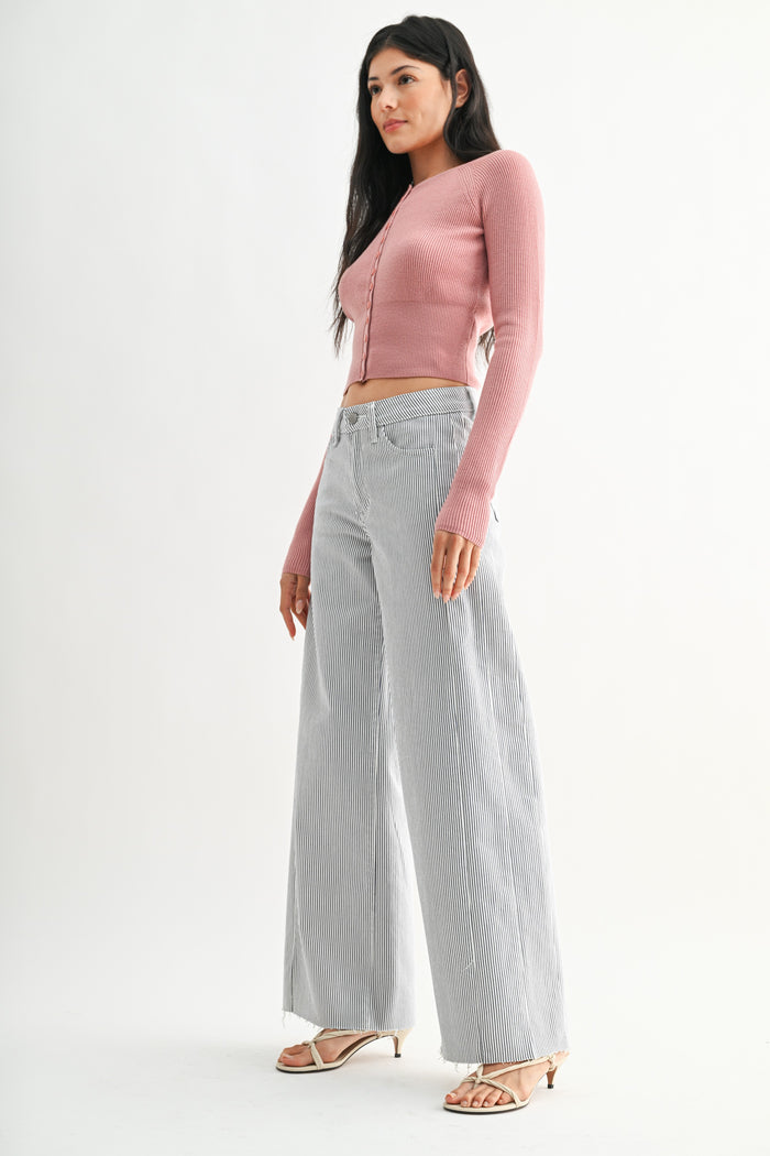 Woman wearing a pink cardigan and light gray pants on a white background