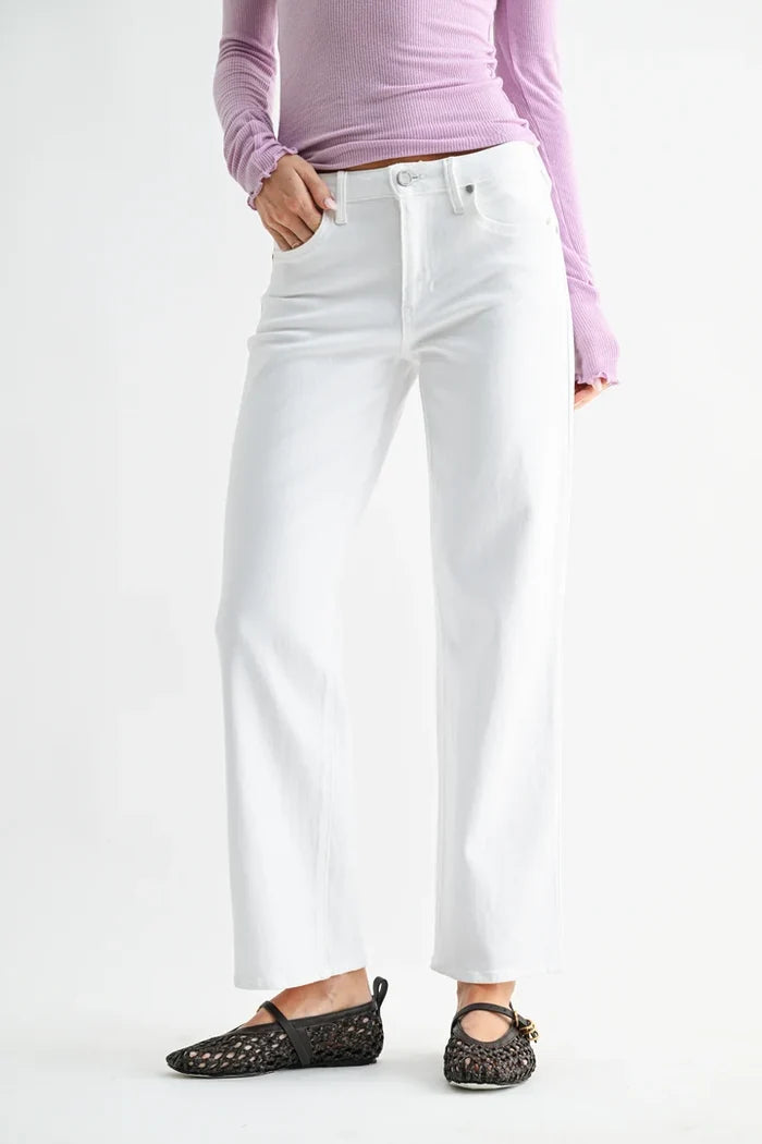 A model wearing white wide-leg cropped jeans, a light purple long-sleeve top, and black woven flats, shown from the waist down against a plain white studio background.