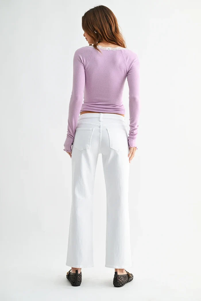 A woman shown from the back wearing a lavender long-sleeve top, white wide-leg cropped pants, and black lace-up flats against a plain white studio background.