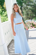 Woman wearing a blue and white striped outfit on a wooden deck with greenery in the background