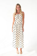 A woman modeling a strapless cream maxi dress with black polka dots, standing against a plain white studio background.