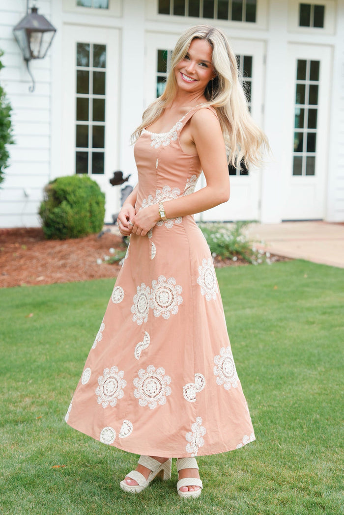 Woman in a peach dress with white floral patterns standing on grass.