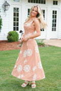 Woman in a peach dress with white floral patterns standing on grass.