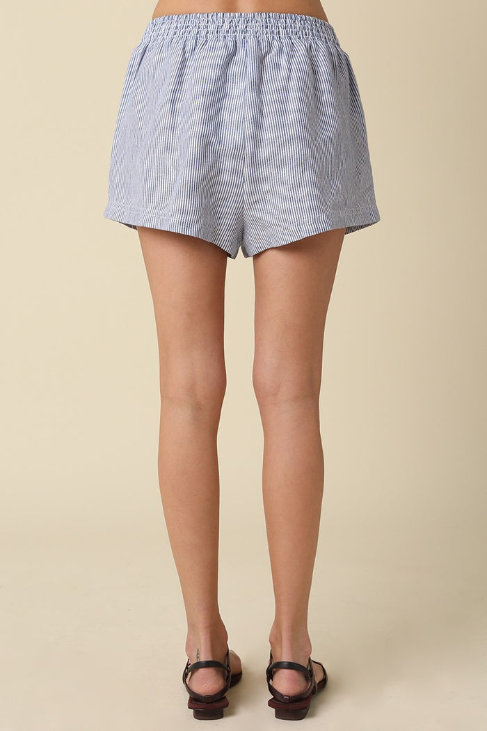 Blue and white striped shorts worn by a person on a beige background
