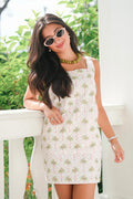 Woman wearing a floral dress with sunglasses and a necklace, standing outdoors.