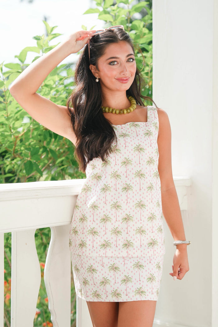 Woman wearing a floral dress standing outdoors with greenery in the background