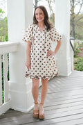 Woman in a polka dot dress standing on a wooden porch with white columns.