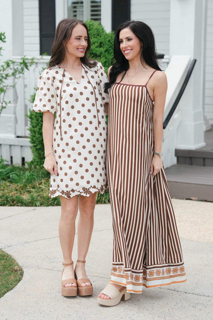 Two women standing outdoors, one in a polka dot dress and the other in a striped jumpsuit.