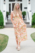 Woman in a floral dress standing on a patio with greenery and a white building in the background