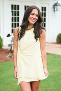 Woman in a light yellow dress standing outdoors with a white building in the background