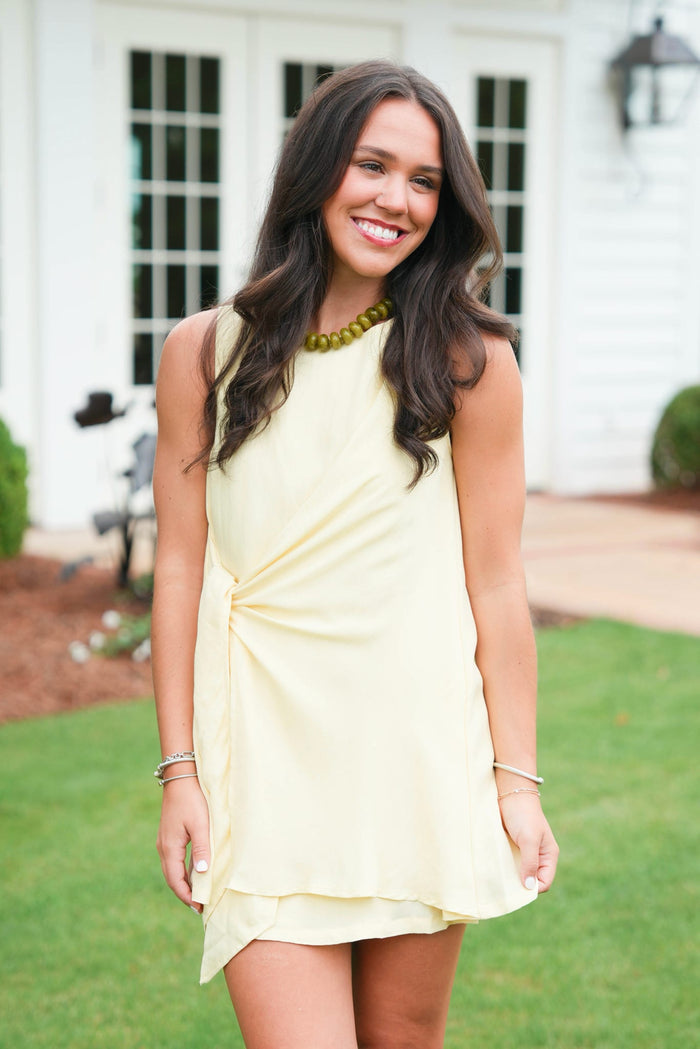 Woman in a light yellow dress standing outdoors with a white building in the background