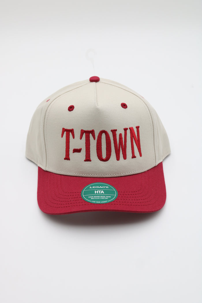 A structured baseball cap with an off-white crown and a red visor, featuring 'T-TOWN' embroidered in red across the front. A green circular HTA sticker is visible on the red visor.
