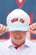A person wearing a white baseball cap with a light blue visor and red embroidered text reading 'OLE MISS', holding the brim down over their eyes.