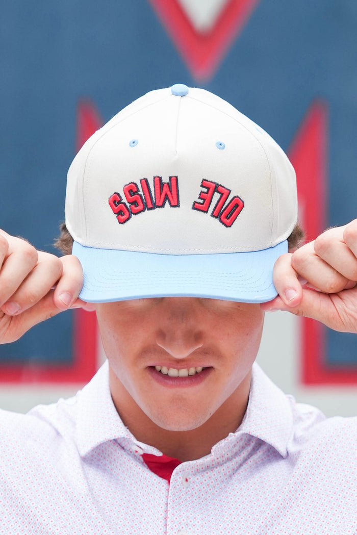 A person wearing a white baseball cap with a light blue visor and red embroidered text reading 'OLE MISS', holding the brim down over their eyes.