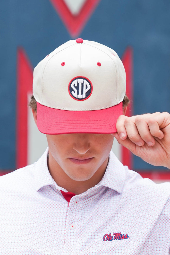 A close-up of a person wearing a white and pink baseball cap with a circular 'SEC' logo on the front, along with a white polo shirt featuring an 'Ole Miss' script logo on the chest.