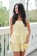 Woman wearing a yellow dress standing on a white railing with greenery in the background