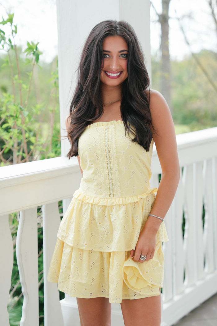 Woman wearing a yellow dress standing on a white railing with greenery in the background