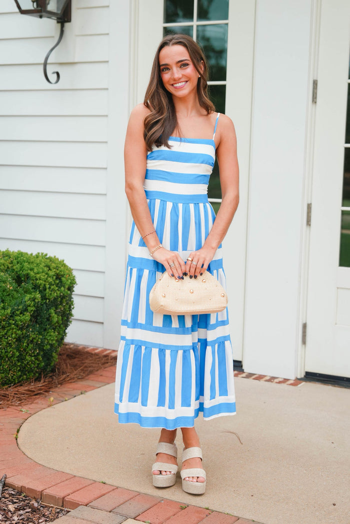 Woman in a blue and white striped dress standing outside a house.
