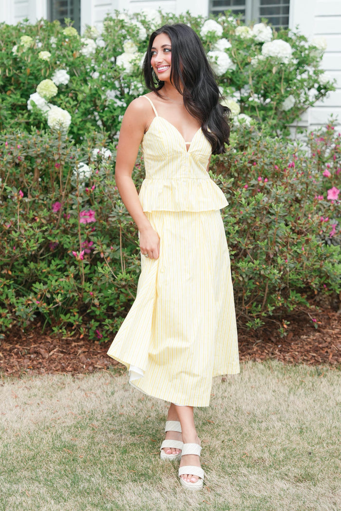 Woman in a yellow dress standing outdoors with greenery and flowers in the background
