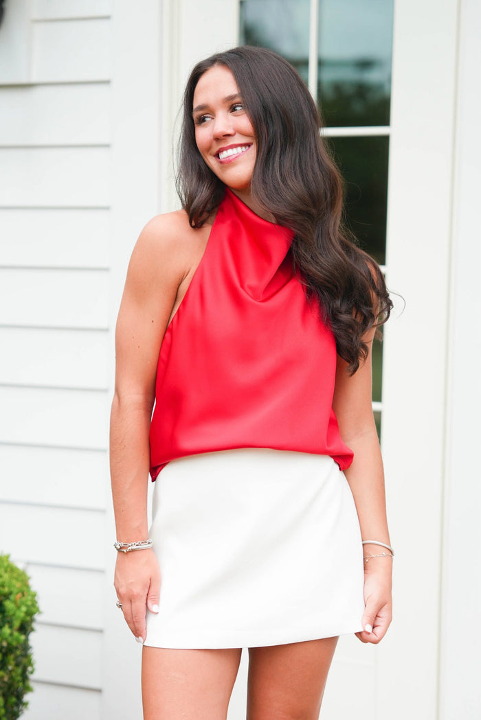 Woman wearing a red top and white skirt standing outdoors.