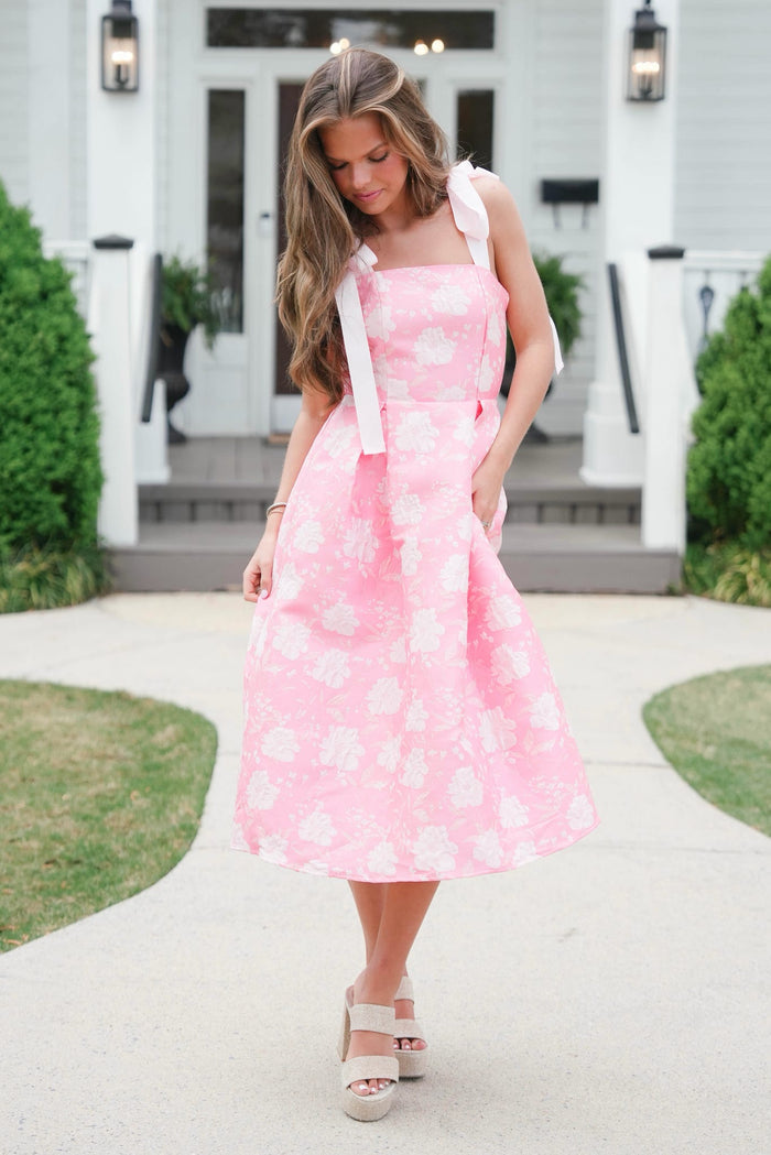 Woman wearing a pink floral dress standing on a sidewalk.