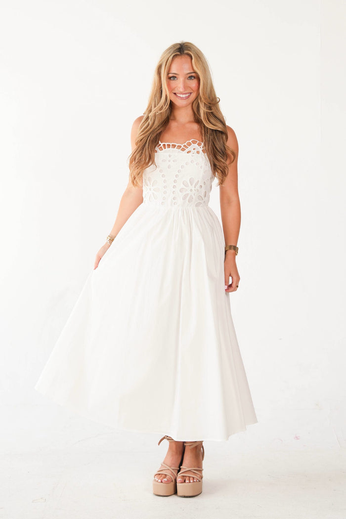 A woman modeling a white strapless maxi dress with a lace bodice and a flowing skirt, paired with beige platform sandals, against a plain white studio background.