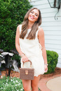 Woman in a white dress holding a wicker handbag outdoors.