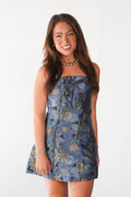 A woman modeling a strapless blue floral mini dress with a gold-toned metallic pattern, set against a plain white studio background.