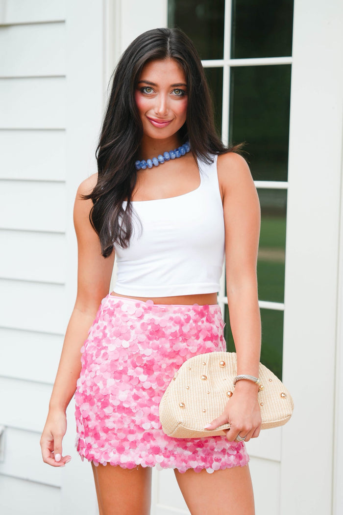 Woman wearing a white top and pink floral skirt with a white background