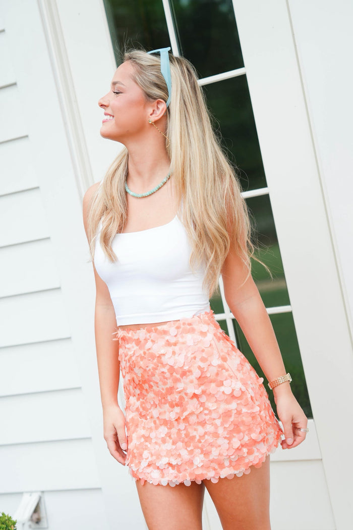 Woman wearing a white top and pink floral skirt outdoors.