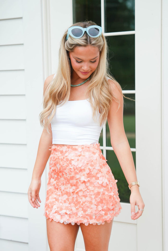 Woman wearing a white top and pink floral skirt with sunglasses on her head.