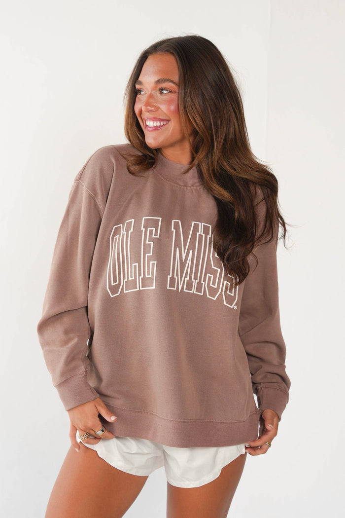 Brunette woman modeling a brown sweatshirt with white lettering and white shorts