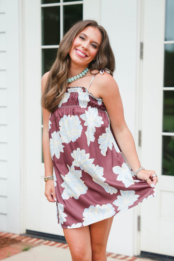 Woman wearing a floral dress standing in front of a white door.