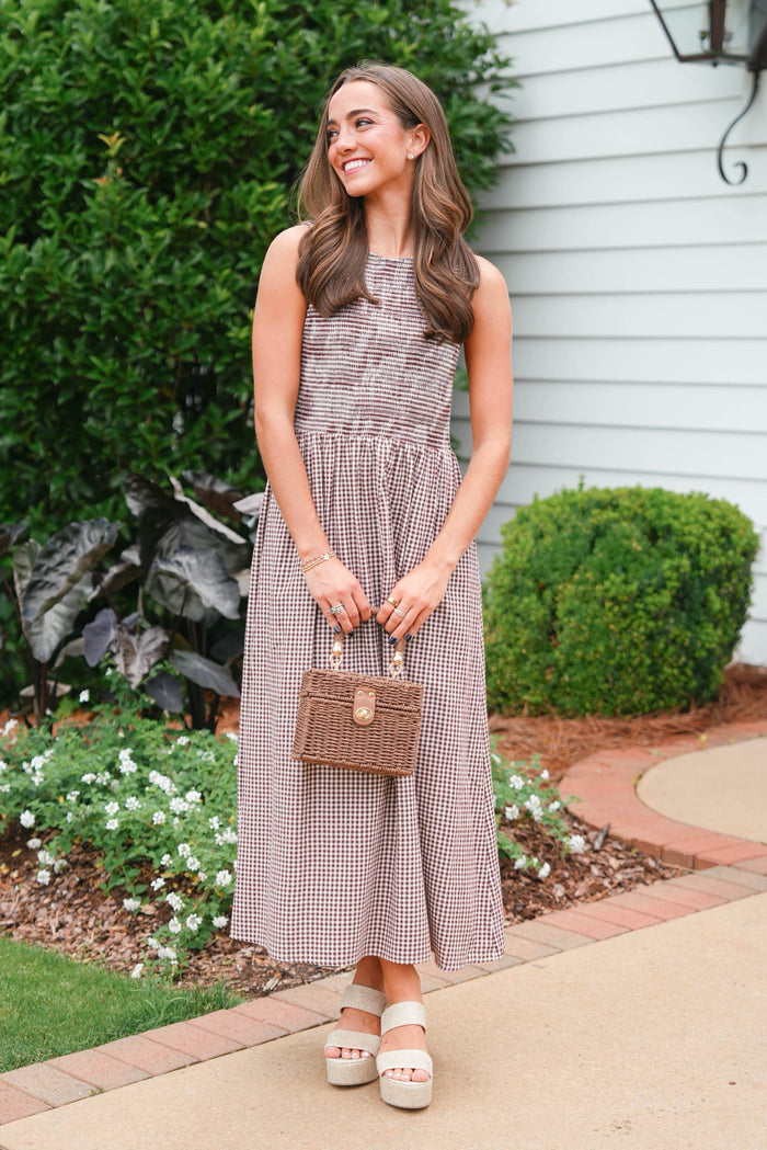 Woman in a checkered dress holding a small bag outdoors.