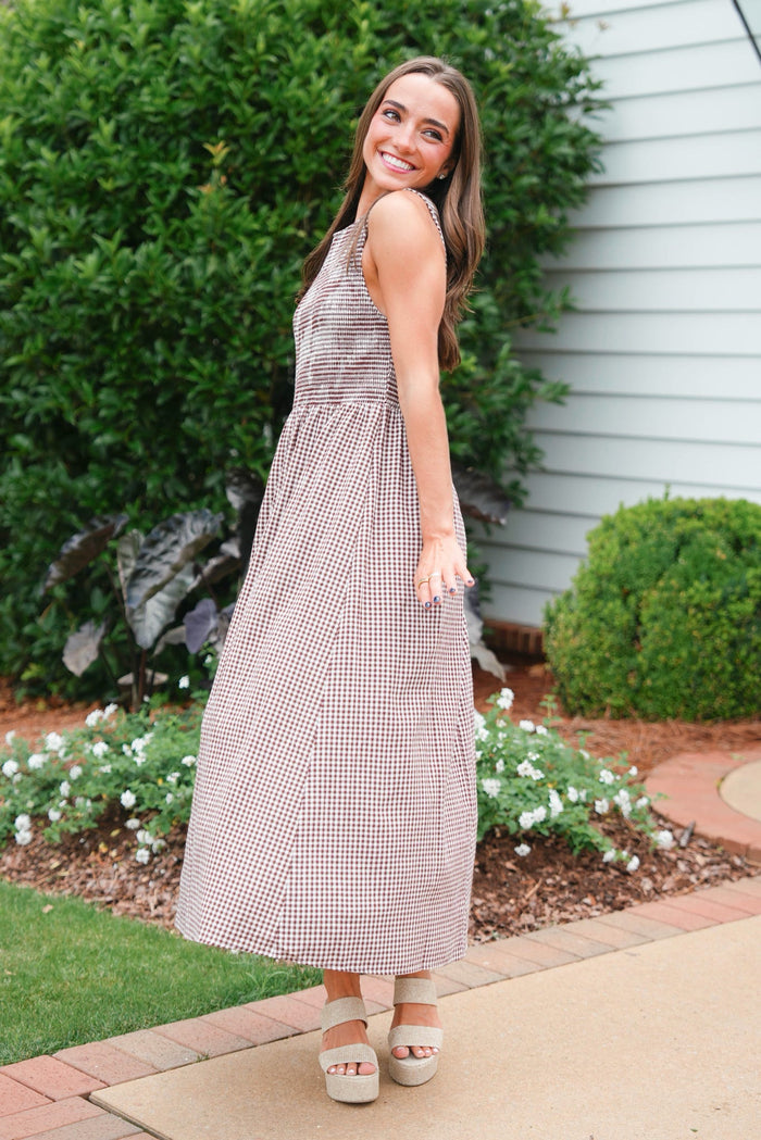 Woman in a checkered dress standing outdoors with greenery and flowers in the background