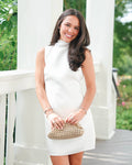 Woman in a white dress holding a woven handbag on a porch