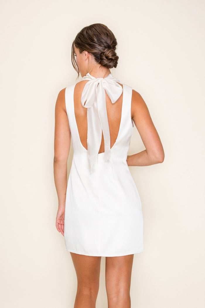 Woman wearing a white dress with a bow detail on the back against a beige background