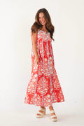 A woman modeling a sleeveless red and white floral maxi dress with vertical blue tie-dye stripes, paired with beige platform sandals, against a plain white studio background.