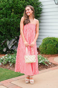 Woman in a red and white striped dress holding a floral clutch outdoors.